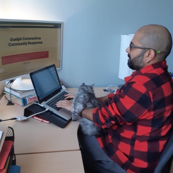 An image of Abhilash sitting, working at his desk alongside his cat.