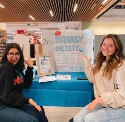 Two students sit in front of table set up for the Psychology society.