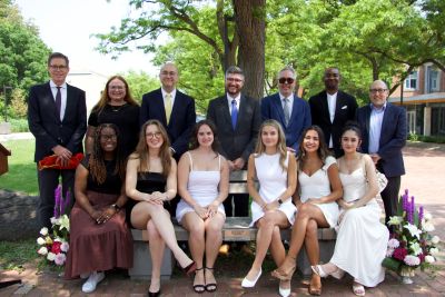 A group photo of JLS students sitting on the bench with professors and mentors standing behind them