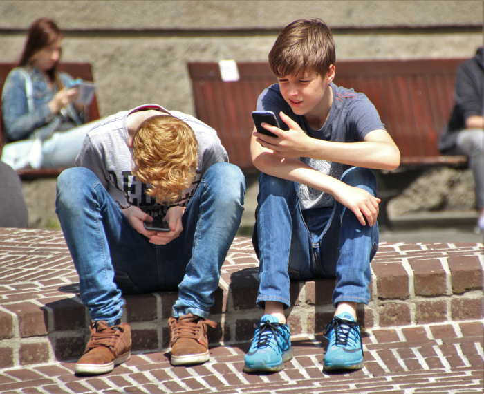 two boys sitting on the curb engrossed in their cell phones on a nice sunny day