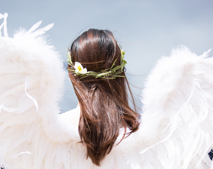 Picture taken from behind of torso and head of woman wearing angel wings. 