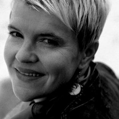 Black and white headshot of Dr. Kerry Preibisch, a person with short, light-coloured hair smiling over her shoulder at the camera.