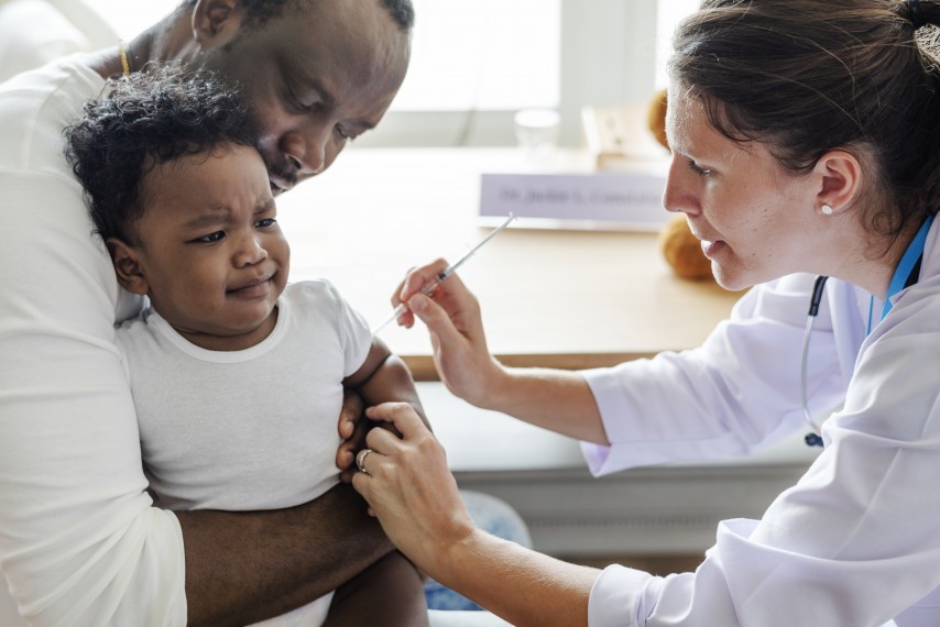 father holds crying young boy as female doctor gives him a needle