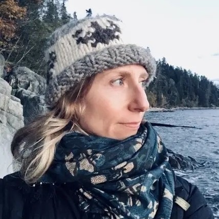 Justine is standing by a lake and wearing a toque and scarf