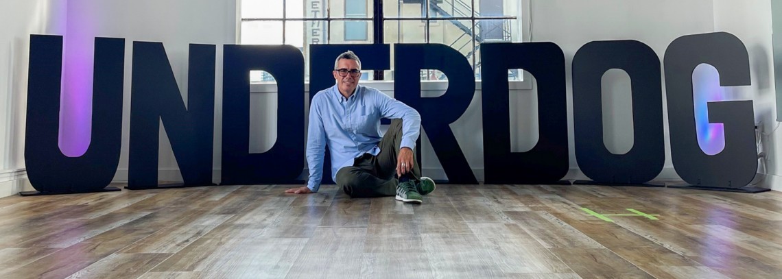 Francesco posing on the floor of a dance studio in front of the word Underdog.