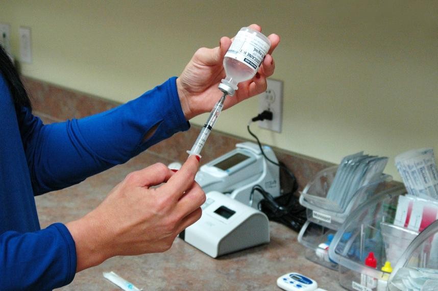 Photo of a person filling a vaccination needle with a vial.  