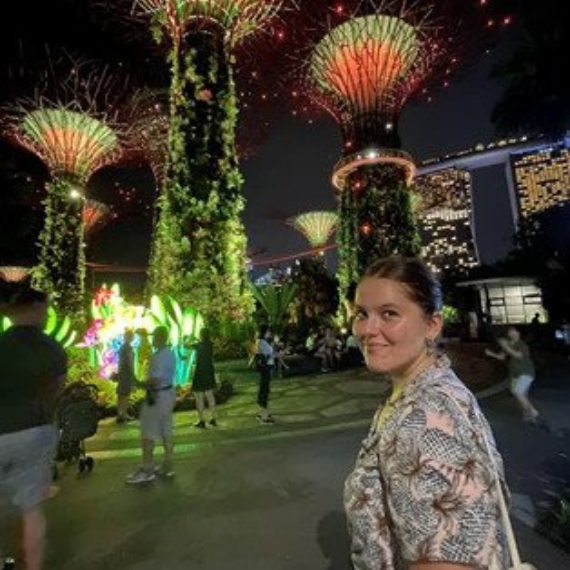 Alara looking back over her shoulder at the camera, behind her large tree-like structures lit up against the night sky.