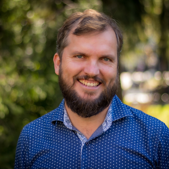 Headshot of Mervyn Horgan, who stands outside with a blue polo shirt and smiles.