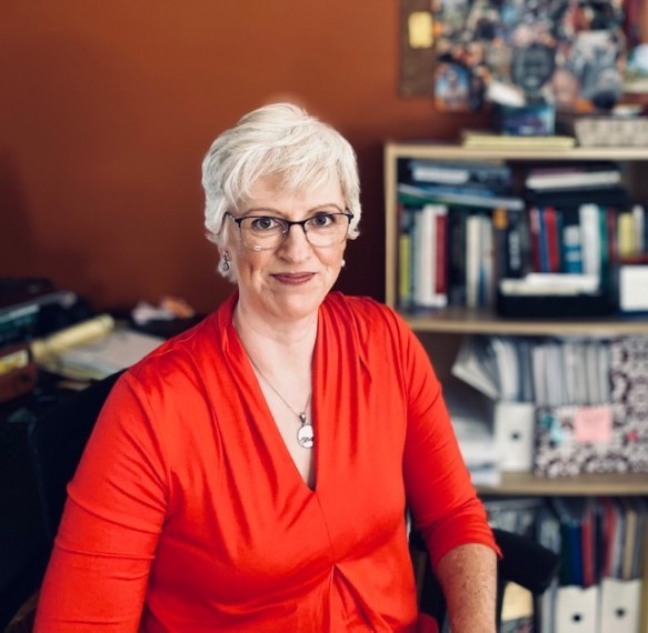 Joanne Garcia-Moores sits in her home office with books on the bookshelf behind her