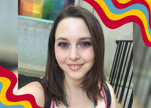 The Looking Glass, Abigail Mitchell is dressed up for pride in a sequin tanktop and mardi gras beads, posing in front of a pride flag.