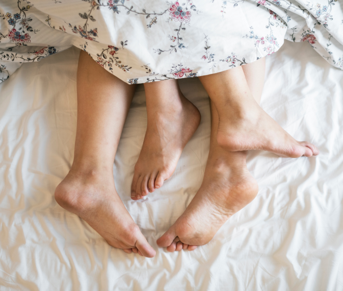 the feet showing sticking out of the blankets of a couple in bed